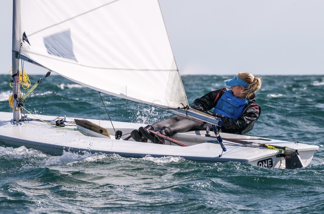 Annie sailing an ILCA upwind in a choppy breeze, 2018.