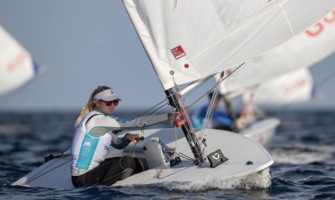 Annie racing her ILCA 6 upwind in a fleet.