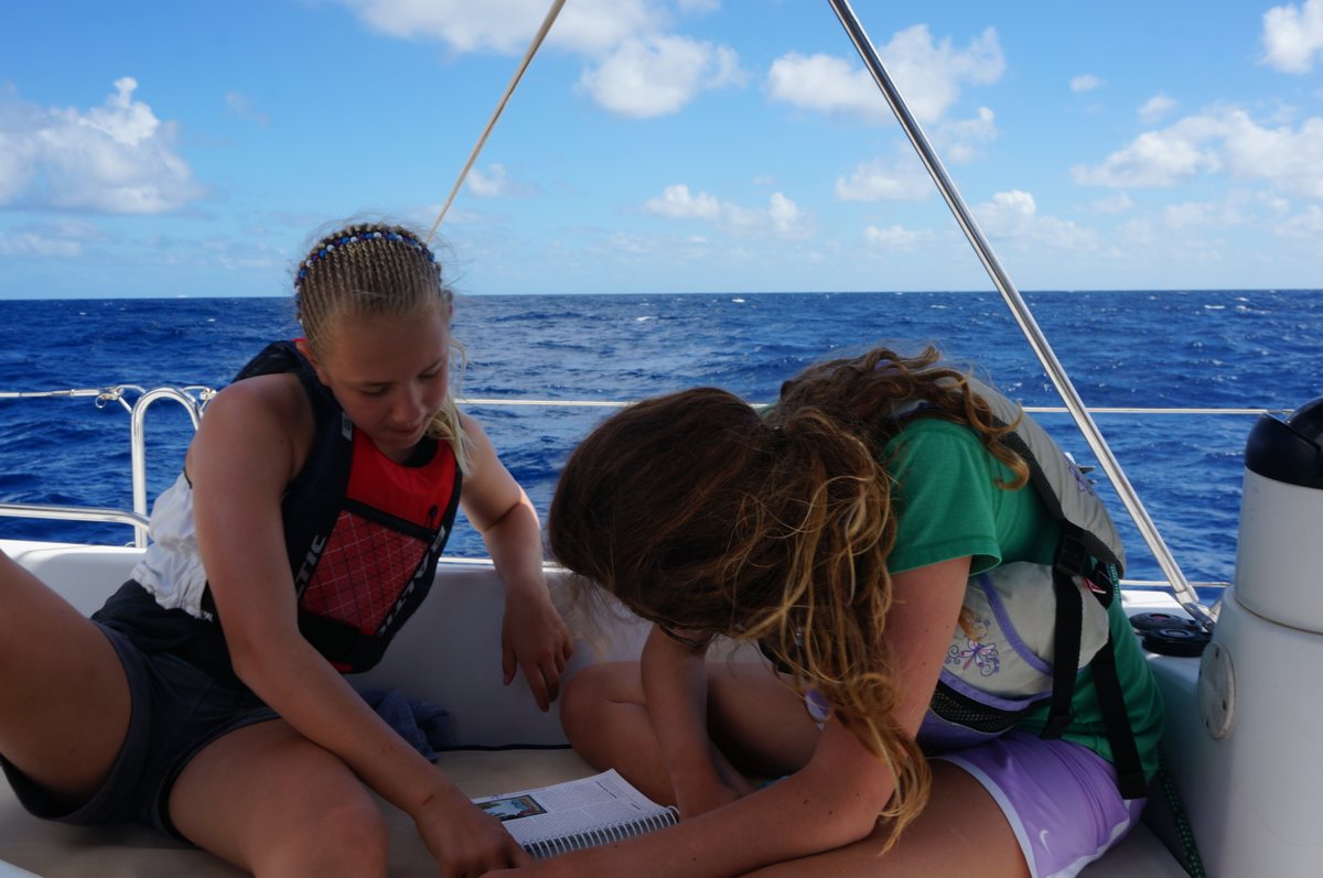 Annie in a life jacket on a sailboat at sea, studying a book during the family sabbatical.